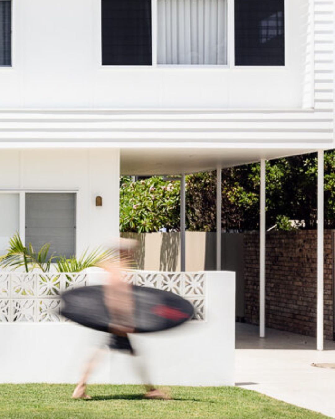 Completed two-storey coastal home with white render facade, wide covered entry, ornate screen wall, and timber framing, representing a custom-designed and council-approved CKS Projects residential build in the Illawarra