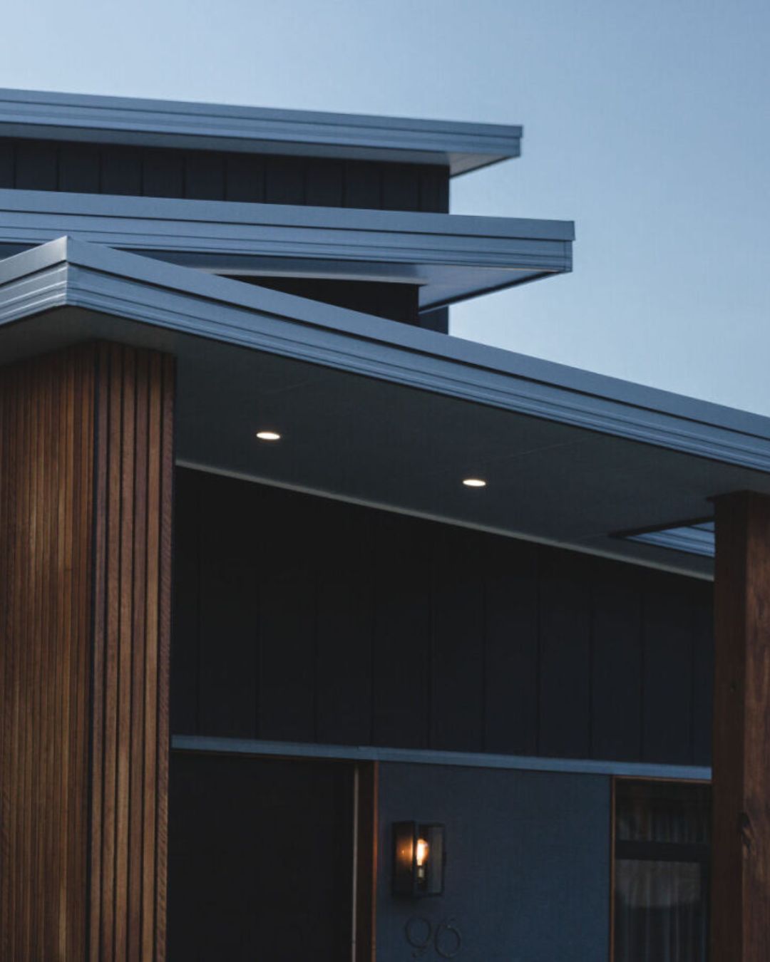 Close-up of a residential home exterior at dusk showing deep eave overhangs and vertical timber battens, demonstrating passive solar design features assessed under BASIX thermal comfort requirements