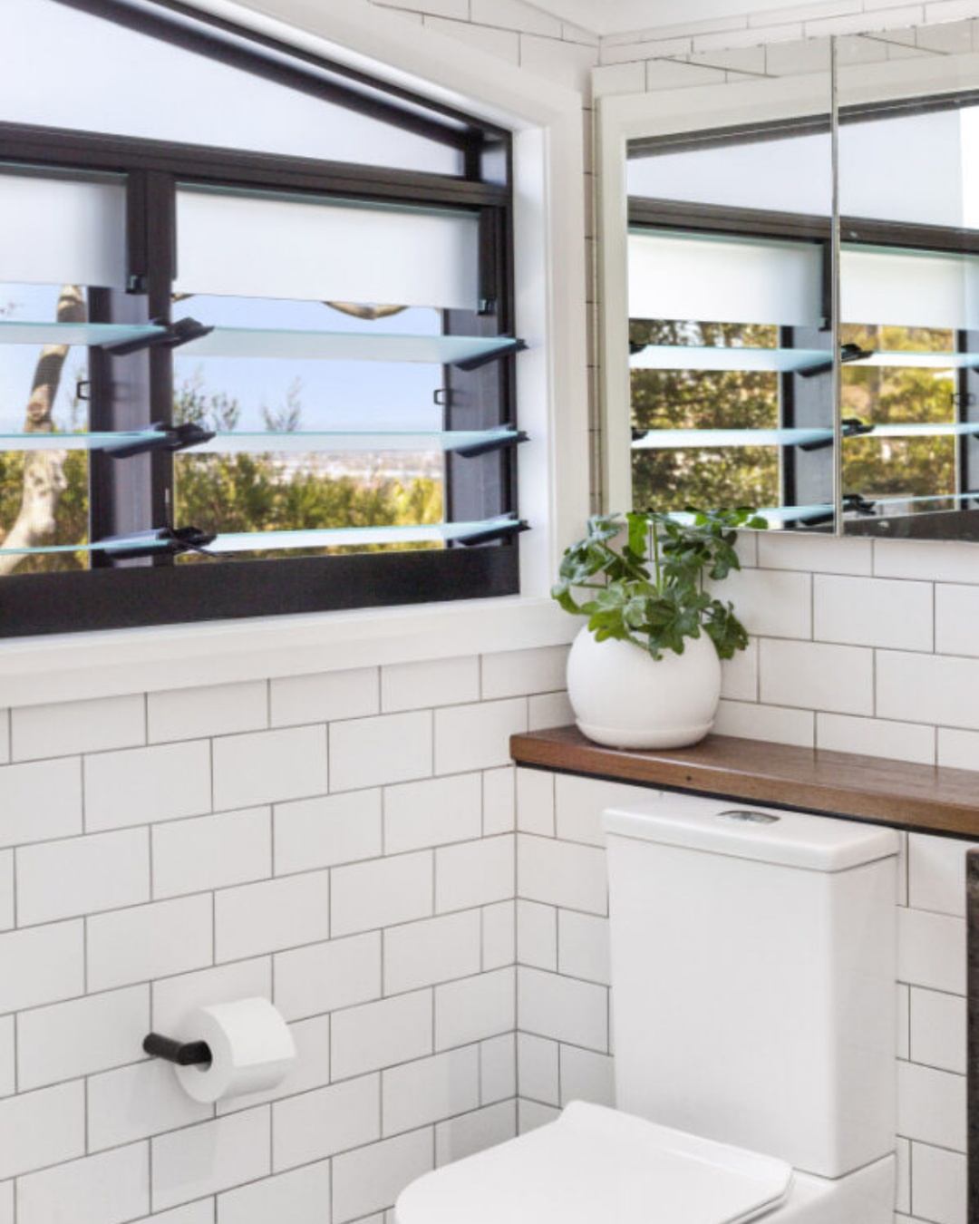 Bathroom interior with louvre glass windows open to Illawarra landscape views and natural cross-ventilation, illustrating passive cooling and water-efficient design principles central to BASIX compliance