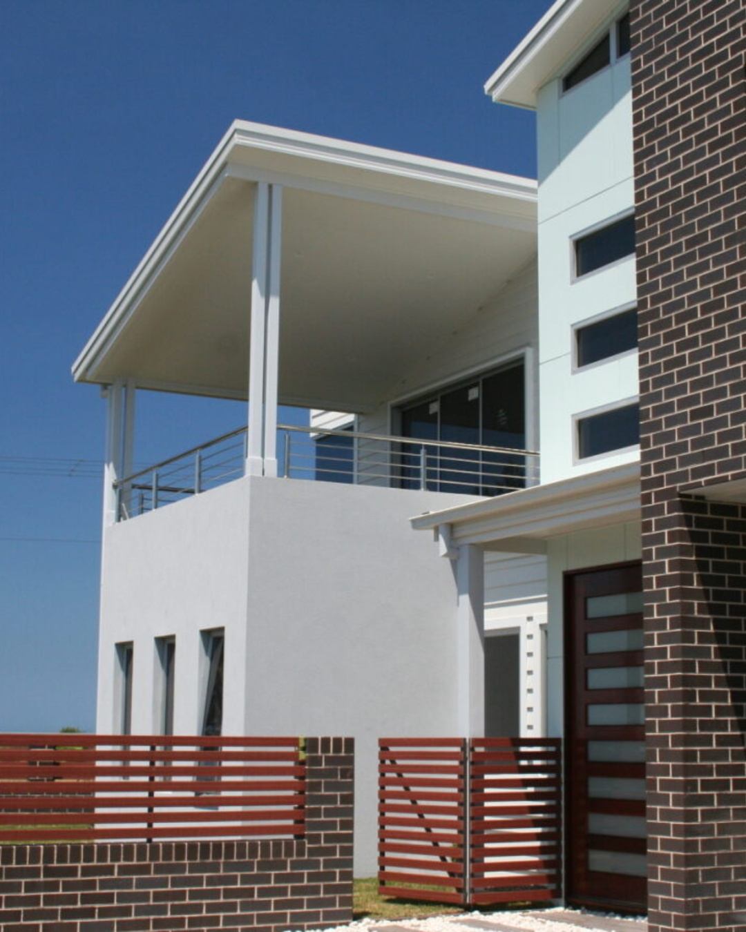 Completed multi-storey residential home in the Illawarra with brick and render facade, upper balcony, timber screening, and clear blue sky, representing a council-approved CKS Projects build ready for occupation