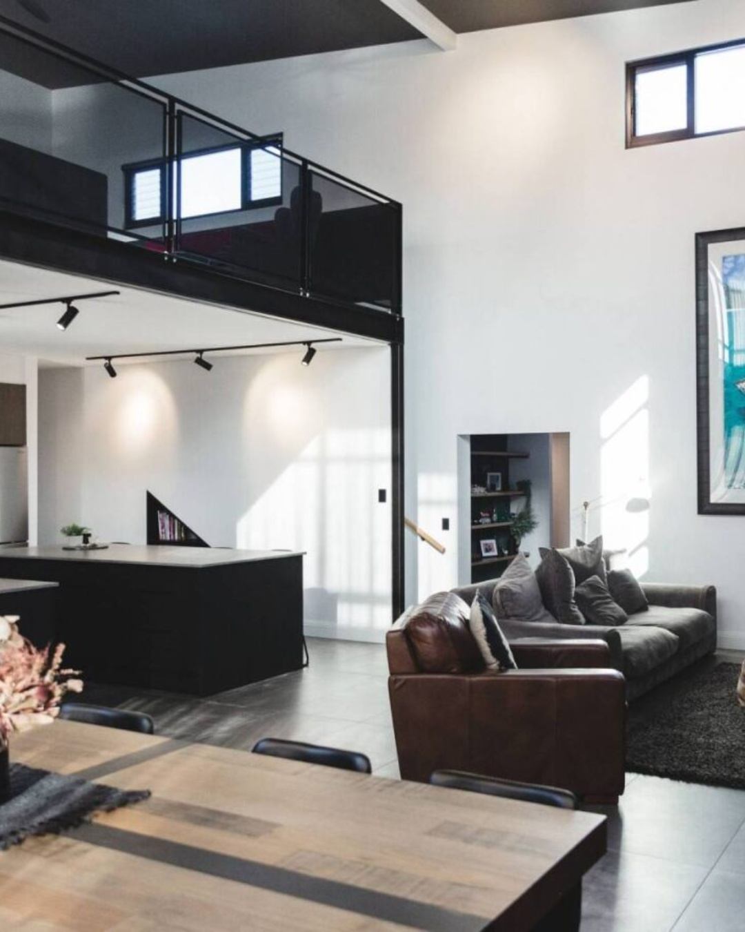 Double-height open-plan interior of a completed CKS Projects custom home in the Illawarra, showing a steel-framed mezzanine, open kitchen, living area, and high clerestory windows, demonstrating the quality of a council-approved, construction-ready build