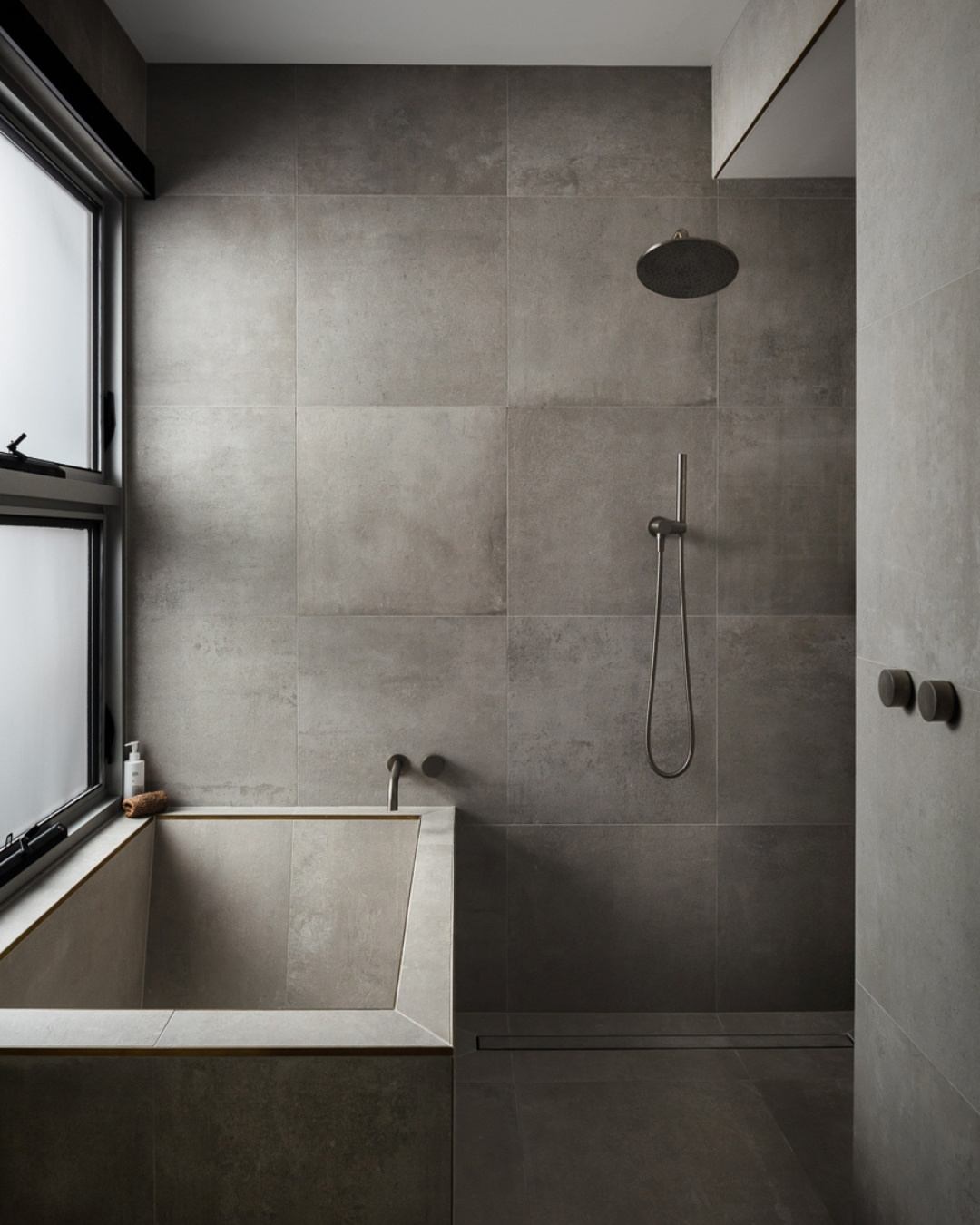 Custom ensuite with large-format grey stone tiles, built-in bath, matte black tapware and rain shower — a cohesive selection outcome
