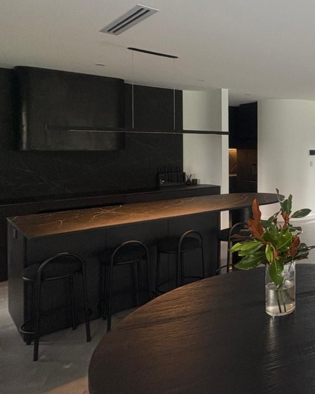 Premium custom kitchen with black cabinetry, stone island bench and brass accents — the result of deliberate, builder-guided material selection