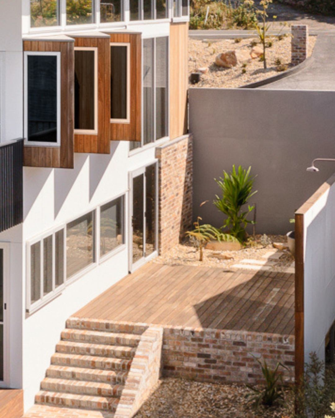 Completed multi-level custom home on a sloped Illawarra block, featuring brick stairs, large windows, and timber cladding — an example of the complex site-aware construction that CKS Projects drafting supports