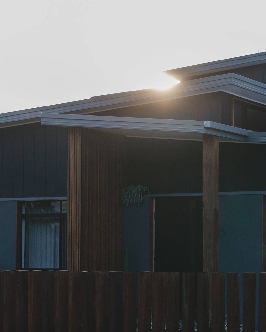 Completed custom home exterior at dusk with dark cladding, timber battens, and timber fence on a residential block