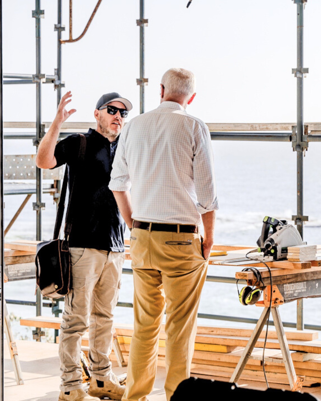 Keiron Moore discussing narrow lot build plans with a client on a coastal Illawarra construction site, with scaffolding and ocean views in the background