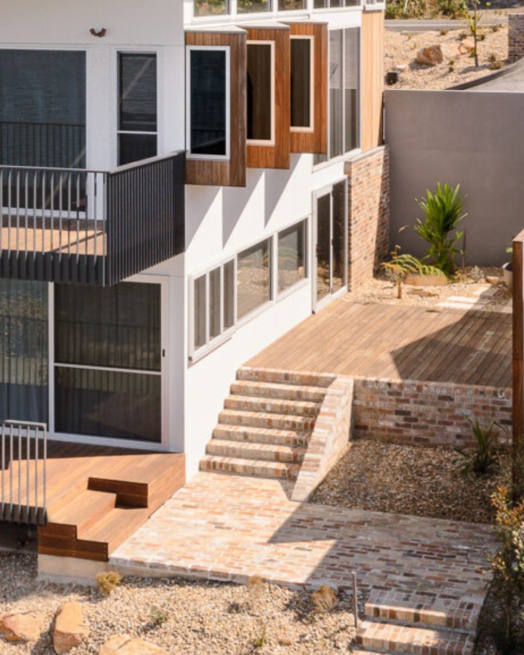 Overhead view of a completed multi-level CKS Projects home on a sloping Illawarra block, showing brick retaining stairs, timber decking at multiple levels, and white render, illustrating the type of site complexity a Pre-DA consultation helps you navigate before committing to plans