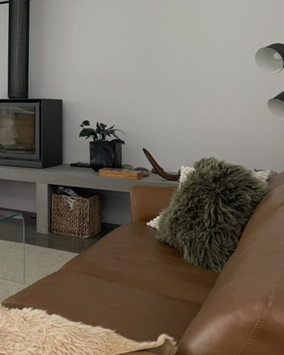 Warm residential lounge interior in a completed CKS Projects build showing a freestanding wood-burning stove on a concrete hearth, terrazzo flooring, tan leather sofa, and natural light, demonstrating the quality of finish achievable in a custom studio home built to the same standard as a full custom dwelling