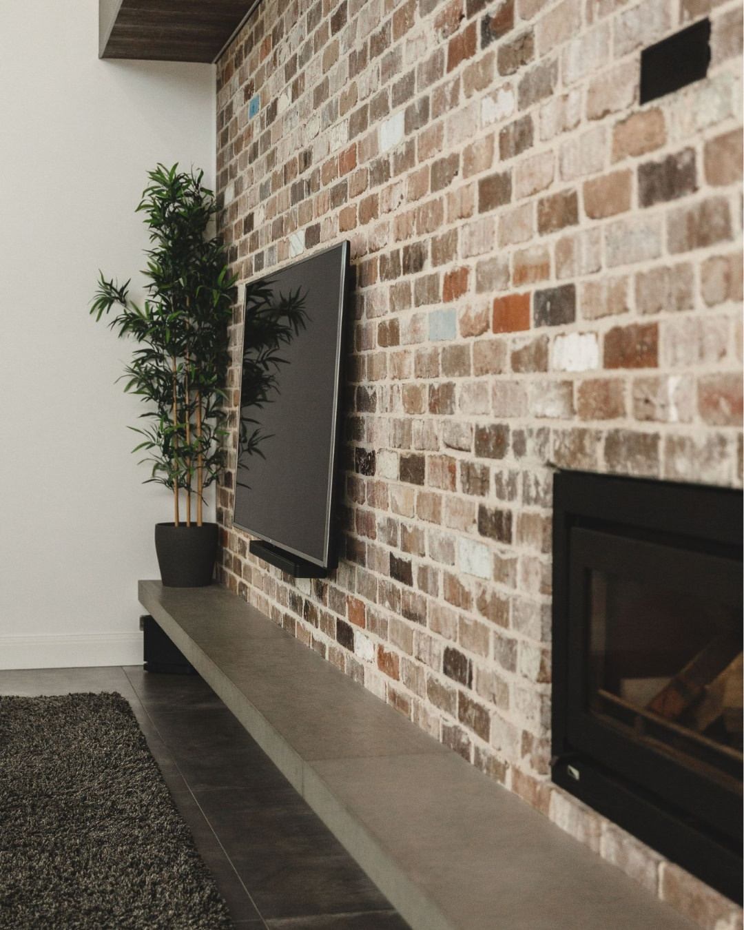 Premium living room interior featuring a recycled brick feature wall, black fireplace with concrete hearth, and high-quality custom finishes