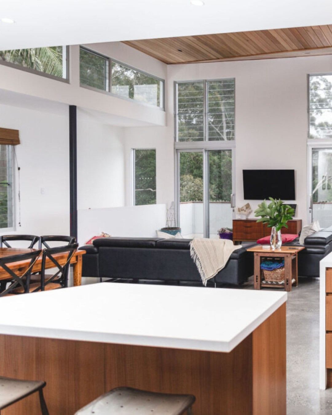 Light-filled open-plan living and kitchen with double-height ceiling, clerestory windows, and timber ceiling panels — the vertical living quality a two-storey home delivers