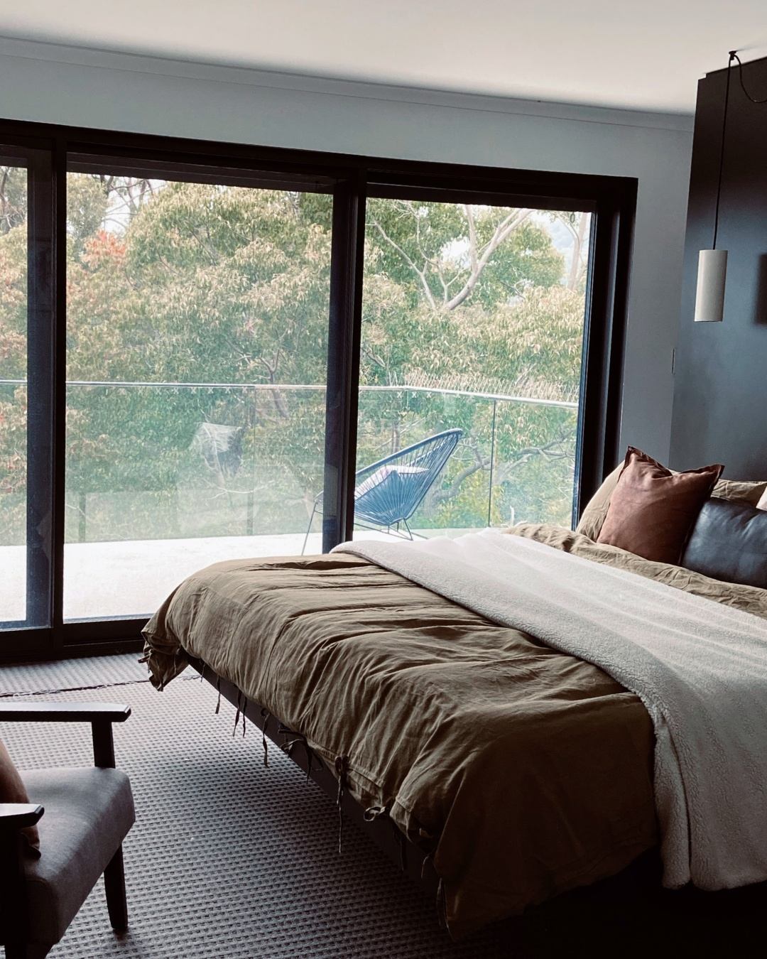 Luxury upper-level master bedroom with floor-to-ceiling windows overlooking leafy native trees — the view and privacy a well-designed second storey delivers