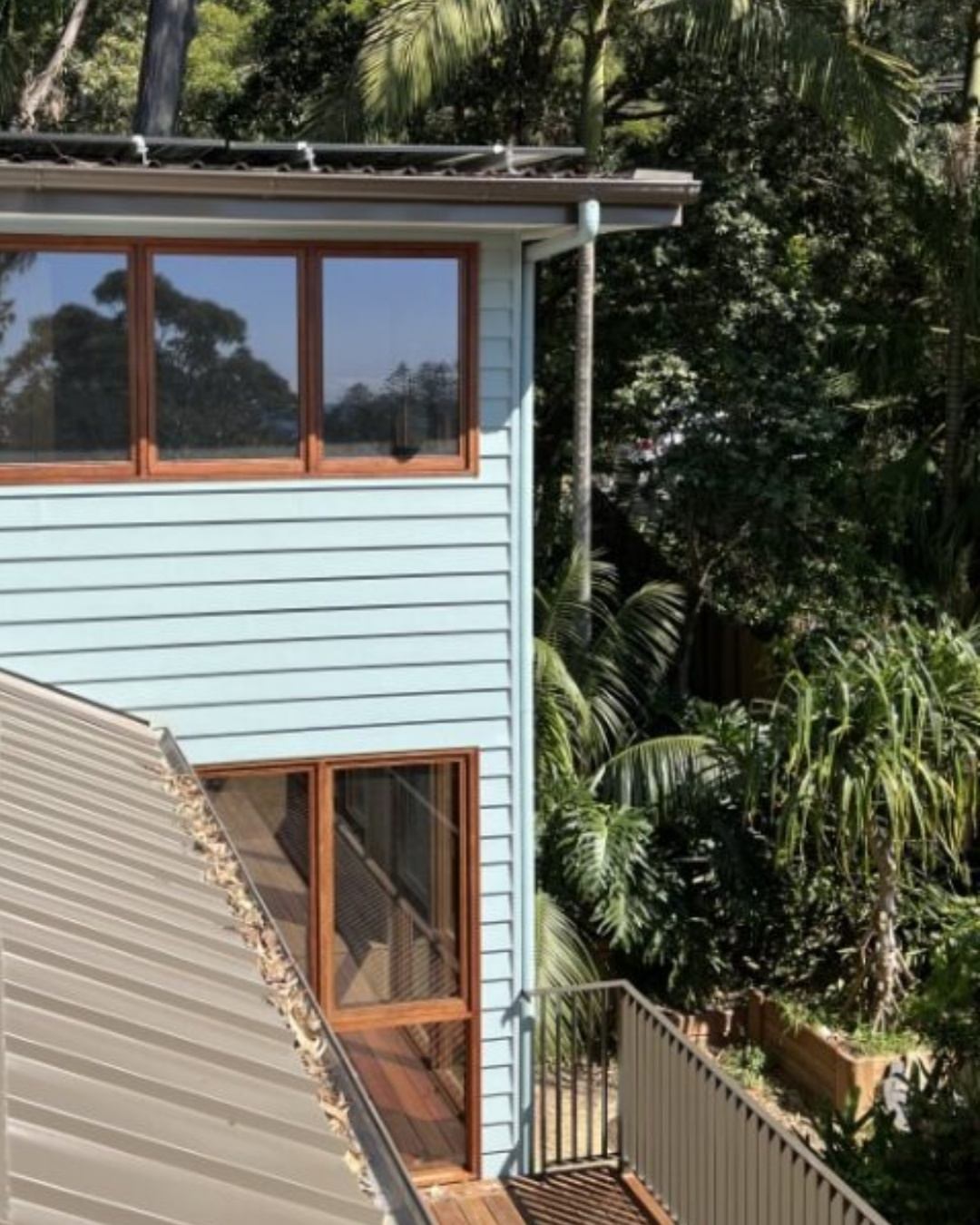 Two-storey weatherboard home on a sloping Illawarra residential site, surrounded by established native gardens